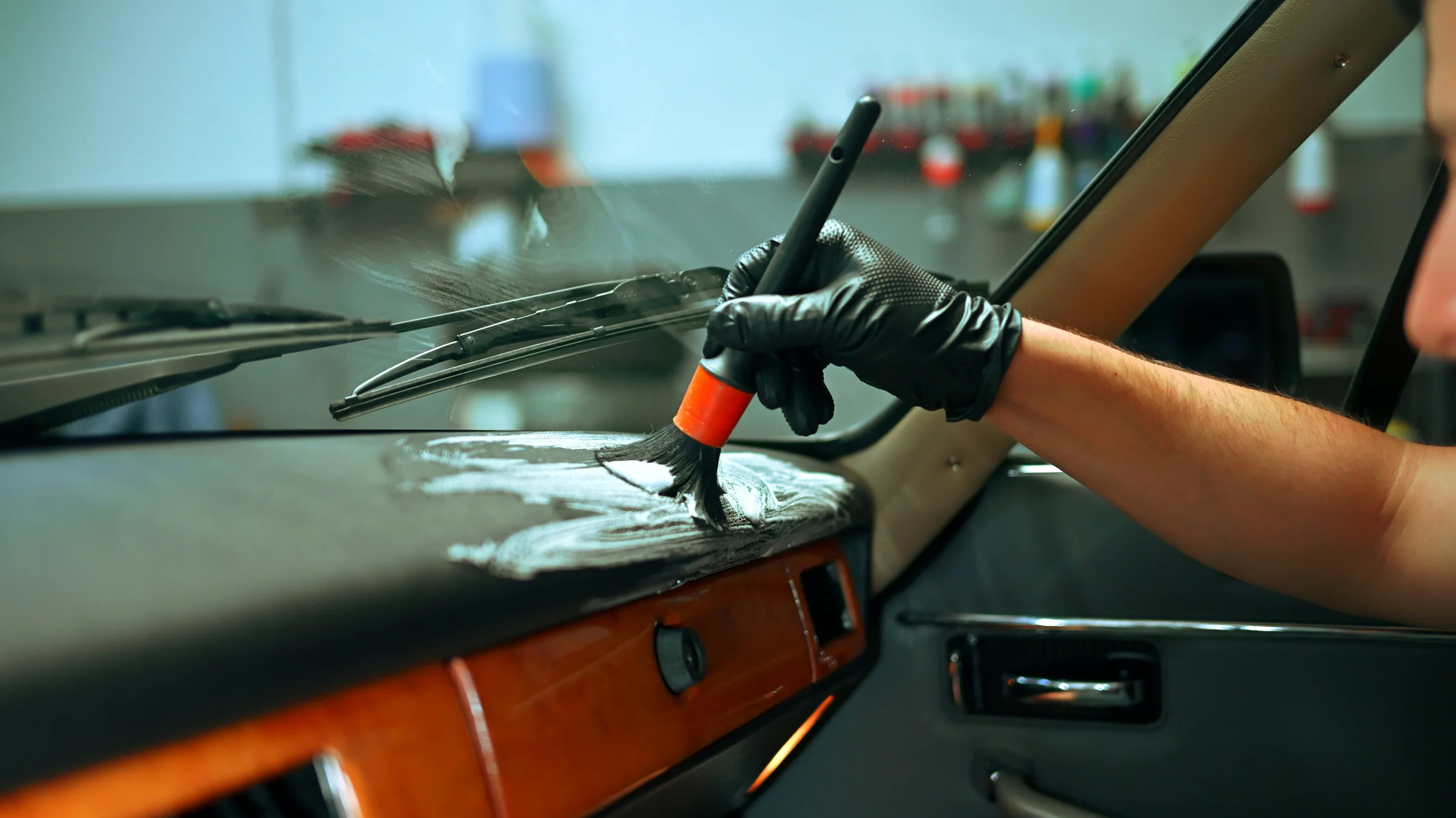 Gloved hand using a detailing brush to clean a vehicle dashboard